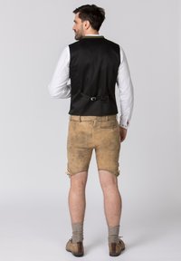 Gilet en satin noir avec un détail de boucle, accompagné de shorts en cuir marron clair avec des accents noués. Des chaussettes et des chaussures complètent l'ensemble.