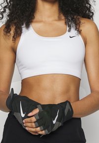 Vit atletisk crop-top med breda axelband, matchad med svarta fingerlösa träningshandskar med grå accentfärger och en vit logotyp.