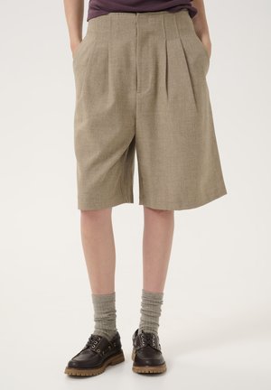 Beige pleated shorts made of textured fabric, featuring side pockets and a relaxed fit, paired with gray socks and brown lace-up shoes.