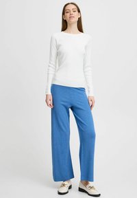 Haut à manches longues blanc à côtes associé à un pantalon large bleu. L'ensemble présente une coupe décontractée et un design simple.