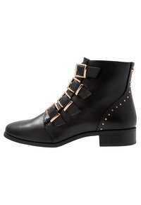 Botte de cheville noire à bout pointu, ornée de cinq boucles dorées et d'accents de clous dorés. Fabriquée en cuir lisse avec un petit talon carré.