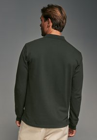 Polo de manga larga verde oscuro visto desde la espalda, con cuello y puños, con una textura suave y corte recto.