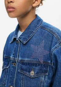 Džínová bunda s ružovým dizajnom hviezdy z kryštálov na ľavom pleci, s kovovými gombíkmi a klasickým prehnutým golierom.