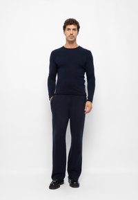 Navyblauer Strickpullover mit langen Ärmeln, kombiniert mit passender weiter Hose aus einem weichen, strukturierten Stoff. Schwarze Schuhe runden das Outfit ab.