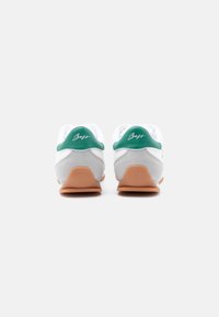 Ζευγάρι λευκά και γκρι αθλητικά παπούτσια με πράσινες λουρίδες στη φτέρνα και καφέ σόλες, σε προβολή από πίσω, σε απλό λευκό φόντο.