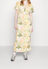 Blommig maxiklänning med V-ringning, korta flirtande ärmar och elastisk midja. Färgerna inkluderar grönt, gult och rosa på en ljus bakgrund.