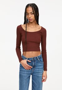 Ruskea pitkähihainen crop-top, jossa on leveä kaula-aukko, valmistettu ribbikankaasta. Yhdistettynä sinisiin korkeavyötäröisiin farkkuihin, joissa on rento malli.