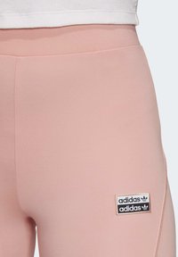 Ljusrosa leggings gjorda av stretchmaterial med en slät yta. Har en svart Adidas-logga på sidan.