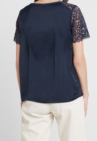 Mörkblå topp med korta spetsärmar och en mjuk textur. Enkel design med rund halsringning och avslappnad passform.