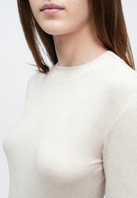 Top bege claro de manga comprida com um padrão texturizado subtil, apresentando um decote redondo e um design ajustado. Tecido suave e bordas sem costura.