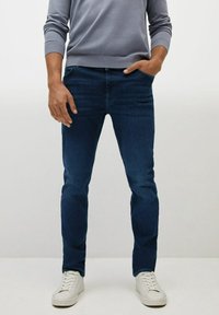 Dark blue denim jeans with a slim fit, five-pocket design, and slight fading. Pairing white sneakers adds contrast to the outfit.