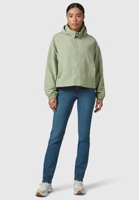 Light green cropped jacket with a hood, two side pockets, and button closures. Worn over blue jeans and white sneakers.