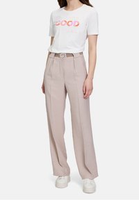 Bílý bavlněný tričko s potiskem "GOOD" v růžové a oranžové, doplněné světle béžovými širokými kalhotami a strukturovaným pásem s kulatou sponou.