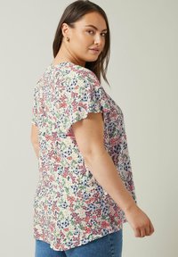 Blumenbluse mit kurzen Schmetterlingsärmeln, aus leichtem Stoff mit einem cremefarbenen Hintergrund, buntem Blumenmuster und relaxed Fit.