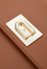 Brun texturerad läderväska med ett guldfärgat metallspänne, med en U-formad design och prägling av logotypdetalj på spännet.