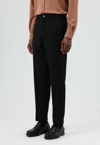 Zwarte op maat gemaakte broek met een rechte pijp, gedetailleerde zakken en een knoopsluiting, gecombineerd met zwarte loafers.