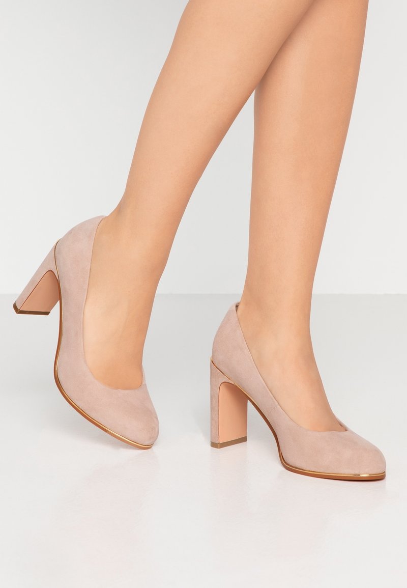 Escarpins en daim beige avec un bout arrondi et un talon bloc. Le talon présente un accent rose clair contrastant et une finition lisse.