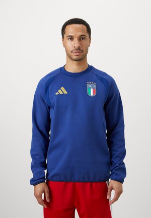 Felpa sportiva blu con scollo rotondo, maniche lunghe, dettagli dorati e logo dell'Italia sul petto. Sono visibili anche pantaloni sportivi rossi.