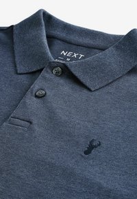 Polo de color azul oscuro hecho de tela texturizada, con un cuello clásico, dos botones negros y un pequeño logo bordado cerca del dobladillo.