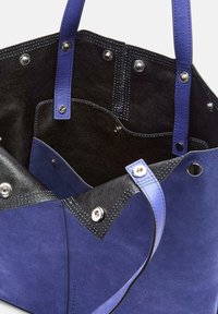 Niebieska i czarna torba tote z zamszu, z srebrnymi zatrzaskami, podwójnymi uchwytami i widoczną kieszenią wewnętrzną.