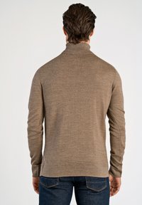 Brun polotröja i stickat material med långa ärmar, slät textur och en något figursydd design, kombinerad med mörkblå jeans.