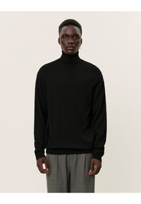 Schwarzer Rollkragenpullover aus einem glatten Strickmaterial, mit langen Ärmeln und taillierter Passform. Getragen mit karierter Hose.