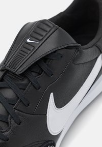 Zapatillas de cuero negro con una lengüeta texturizada, cordones negros, logo de Nike blanco y un acento blanco a lo largo de la suela.