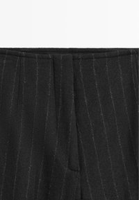 Detailní záběr na černou látku s jemným proužkováním, která má vertikální světle šedé pruhy a středový šev.