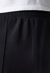 Pantalones cortos de textura negra con cinturilla elástica, de ajuste casual y costuras laterales visibles, parcialmente ocultos por una camisa blanca.