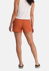 Oranje sportshorts met een gladde textuur, elastische tailleband en een gecropt wit tanktop. Gedragen met zwarte slippers.