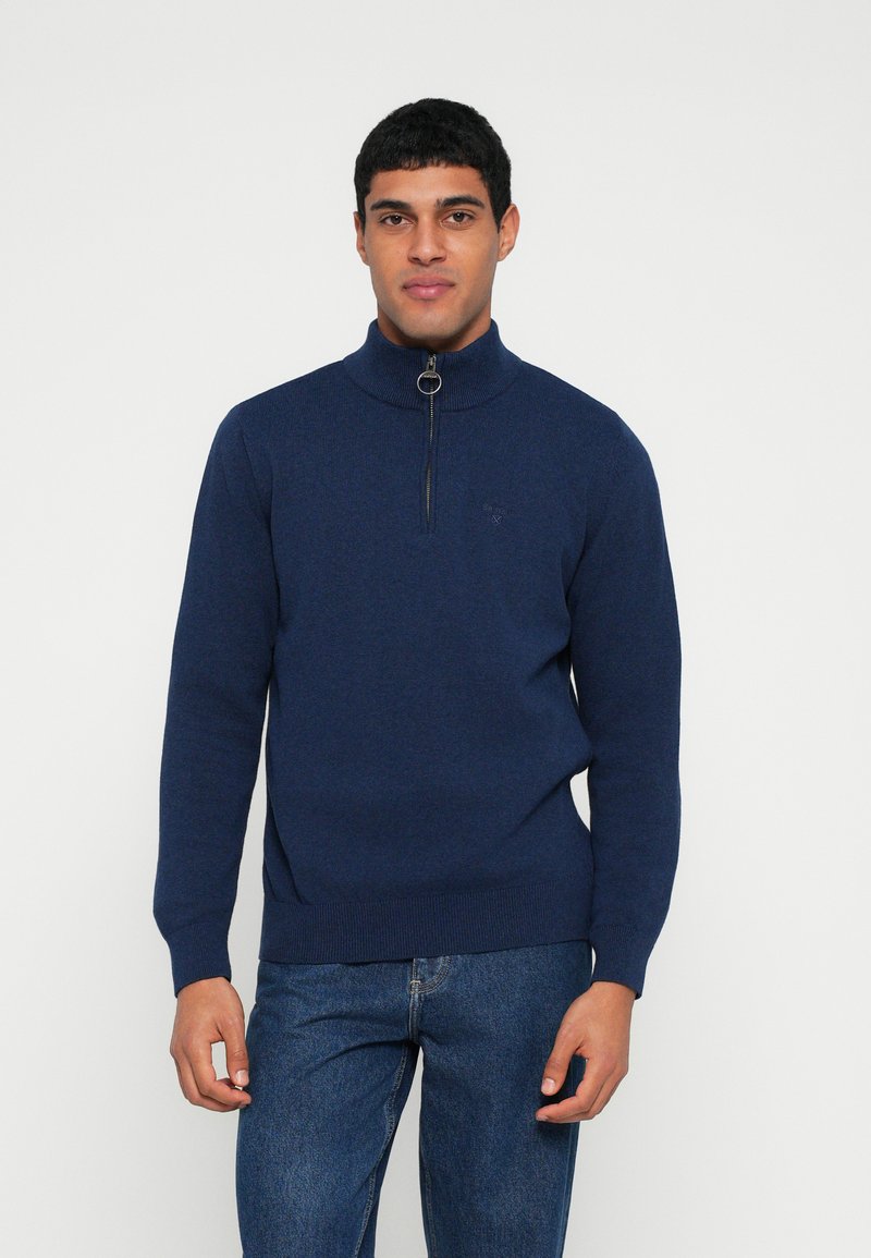 Camisola de malha azul-marinho com gola alta e fecho de correr de um quarto. Apresenta punhos e bainha canelados, com um detalhe sutil do logótipo.