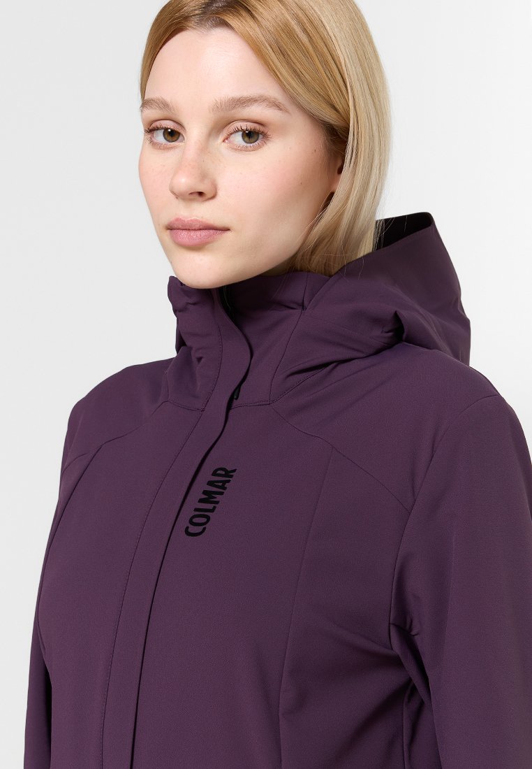 Giacca softshell viola con collo alto e zip nera. Presenta il logo Colmar sulla parte anteriore. Texture liscia, design minimalista.