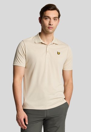 Polo beige con maniche corte, dotato di colletto e di un logo a forma di farfalla gialla sul lato sinistro del petto. Tessuto morbido e design aderente.