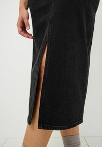 Svart denimkjol med en sidofåra, som har en strukturerad form och synlig sömnad. Tyget har en subtil textur som förstärker dess design.