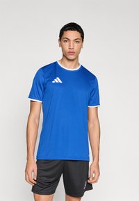 Camiseta deportiva azul con ribete blanco, manga corta y logotipo de Adidas en el pecho izquierdo, combinada con pantalones cortos negros. Material liso y ligero.