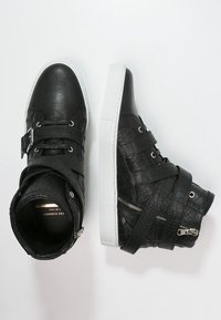 Czarne, teksturowane sneakersy typu high-top z białymi podeszwami, detalem zamka, klamrą oraz krzyżującymi się paskami na białym tle.