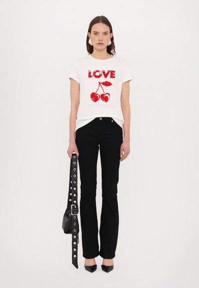 T-shirt bianca con grafica rossa "LOVE" e ciliegia, abbinata a pantaloni neri svasati e una borsa nera con tracolla borchiata, indossata con scarpe a punta.