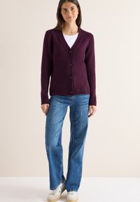 Cardigan bordeaux con chiusura a bottoni, polsini e orlo a costine. Abbinato a jeans blu a gamba larga e sneakers bianche con accenti chiari.