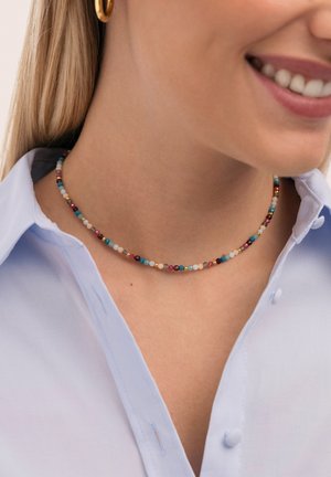 Collar choker colorido con pequeñas cuentas redondas en turquesa, rojo, dorado y blanco, mostrando un patrón constante a lo largo de una cuerda delgada.