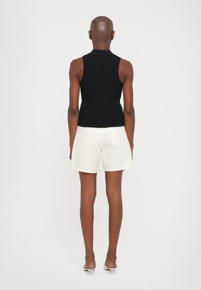Black ribbed sleeveless top paired with cream shorts, featuring a smooth texture and simple design. The shorts have two back pockets.