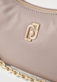 Borsa in nylon beige chiaro con logo in metallo dorato, zip dorata e tracolla a catena robusta. Texture liscia con una leggera lucentezza.