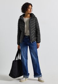 Svart puffjacka med huva, vadderad textur; ljusgrå tröja; vida blå jeans; svart tote-väska; vita sneakers.