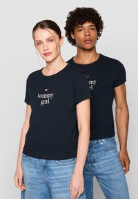 Kariniai medvilniniai marškinėliai, kurie turi apvalią kaklo iškirptę, trumpas rankoves ir siuvinėtu "tommy girl" logotipu su raudona žvaigždute ant krūtinės.