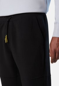 Pantalones de chándal negros con cordón en la cintura, cuentan con bolsillos laterales, costuras en contraste y un logotipo texturizado en la pierna izquierda.