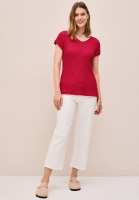 Top corto de punto texturizado rojo, con cuello redondo, combinado con pantalones rectos blancos y zapatos de lona beige.