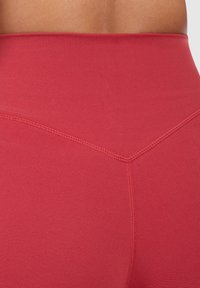 Hoogwaardige rode leggings gemaakt van rekbaar materiaal, met platte naden en een driehoekig stikpatroon op de achterkant.
