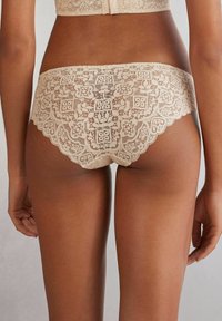 Spetsunderkläder i beige färg, med blommönster, vågiga kanter och en mjuk textur. Designade för en bekväm passform.
