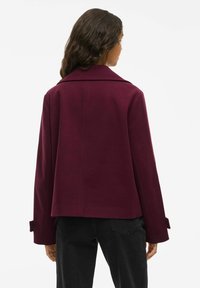 Bordowy płaszcz z mieszanki wełny z wyłogami i szerokimi rękawami, charakteryzujący się luźnym krojem i zapinanymi mankietami.