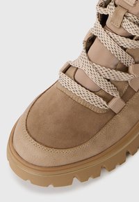 Brown suede hiking boot featuring woven, light-colored laces and a textured rubber sole with defined treads, designed for traction.