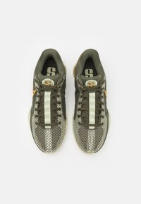 Chaussures de sport vertes et beige avec une tige en mesh texturé, présentant une bande vert clair et un accent jaune, design à lacets et semelle coussinée.